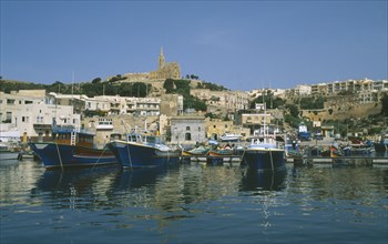 MALTA, Gozo, Mgarr, Fishing boats in harbour overlooked by cathedral.