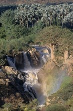 NAMIBIA, Epupa Falls, Water gushing through layers of rocky cliffs into fast flowing river below.