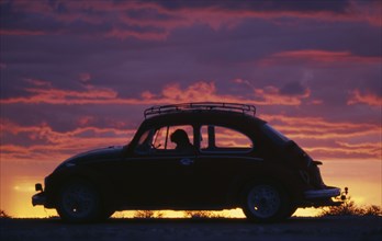 NAMIBIA, Transport, VW Beetle in silhouette against dramatic sunset sky.