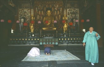 SOUTH KOREA, Kyansu, Pulguk-Sa temple.  Interior with worshippers praying in front of seated Buddha