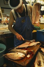 JAPAN, Honshu, Tokyo, Tsukiji Fish Market with man slicing a fish in half