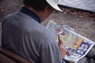 JAPAN, Honshu, Hiroshima, View over the shoulder of a man reading the newspaper with a magnifying
