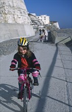CHILDREN, Playing, Young girl on a bicycle dressed in protective cycling helmet and pads riding on