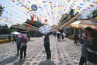 CHINA, Yunnan, Kunming, People walking on a path holding umbrella’s in Daguan Park with colourful