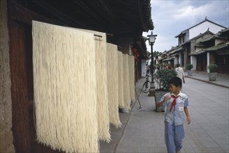 CHINA, Yunnan, Dali., Weishan. Racks of noodles hanging out to dry in street with a boy walking