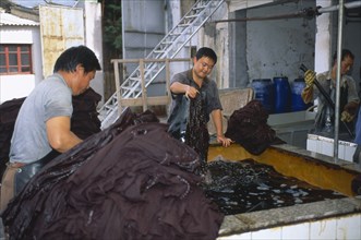 CHINA, Yunnan , Dali, Weishan. Batik factory with men dipping cloths in vats of dye.