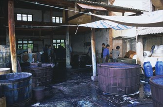 CHINA, Yunnan , Dali, Weishan. Batik factory with men working around  vats of dye under ornings.