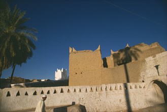 LIBYA, Ghadames Oasis, Man walking past whitewashed wall with mud brick town walls and white mosque
