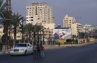 GAZA STRIP, Gaza City, Children on quiet road with billboard of Yasser Arafat and city buildings