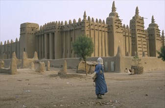 MALI, Djenne, Exterior of mud mosque with man crossing barren ground in the foreground.