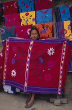 MEXICO, Chiapas, Zinacantan, Young girl holding up brightly coloured embroidered local cloth for