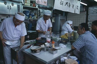 JAPAN, Honshu, Tokyo, Tsukiji Fish Market. Chefs working in the open kitchen of a food bar with