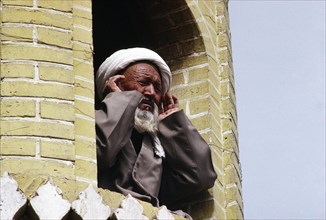 CHINA, Xinjiang Province, Kashgar, Muezzin at call to prayer from minaret of mosque.