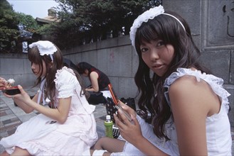 JAPAN, Honshu, Tokyo, Harajuku District. Two teenage girls sitting together with one eating and the