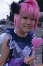 JAPAN, Honshu, Tokyo, Harajuku District. Portrait of a teenage girl with pink hair and several
