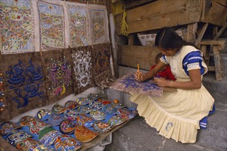MEXICO, Puebla, Taxco, Young woman painting design on piece of bark with masks and other paintings