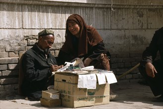 CHINA, Xinjiang, Kashgar, Woman dictating to letter writer at stall outside post office.