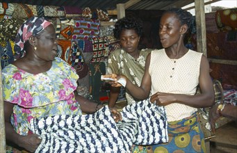 GHANA, West, Markets, Woman purchasing length of batik dyed cloth with fish design from market