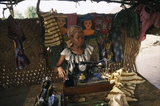 GHANA, Cheroponi, Dressmaker using an old Singer sewing machine in her workshop surrounded by