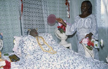 GHANA, Religion, Funeral, Deceased woman lying in state at funeral with female attendant.  This is