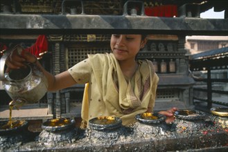 NEPAL, Swayambunath, "Young girl filling butterwick candles in shrine dedicated to Hariti, known