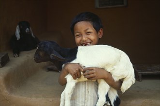 NEPAL, Dhankuta, Smiling young child holding lamb.