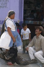 MEXICO, Oaxaca State, Tlacolula, Market day.  Woman holding turkey talking to man in street with