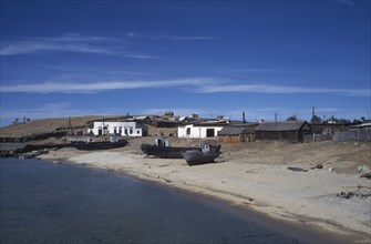 RUSSIA, Siberia, Lake Baikal, Fishing boats pulled up on lake shore with scattered buildings behind