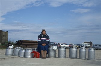 ESTONIA, Baltic Coast, Woman sitting on milk cans waiting for ferry.