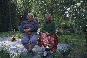 ESTONIA, Kihnu Island, Two peasant women seated on bench in graveyard.
