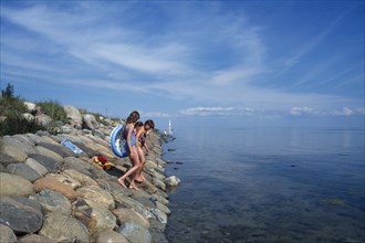 ESTONIA, Kihnu Island, Group of young girls wlking down stone sea defence into water off the Baltic