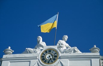 UKRAINE, Odessa, Ukranian flag flying from town hall above clock face and between two statues.