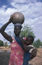 BURKINA FASO, Children, Woman breastfeeding child in sling at her side while carrying water pot on