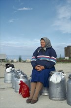 ESTONIA, Work, Woman sitting on milk cans waiting for ferry on the Baltic Coast.