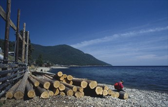 RUSSIA, Siberia, Lake Baikal, Person sitting on length of cut timber on lake shore.