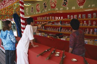 JAPAN, Honshu, Chiba, Narita.  Young couple at shooting range pointing out prizes available to win.