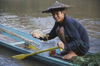 LAOS, Luang Prabang, Fisherman  crouched on wooden canoe on the Mekong River holding up fish.
