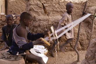 MALI, Weaving, Child weaving on hand loom in Dogon village with other children behind.
