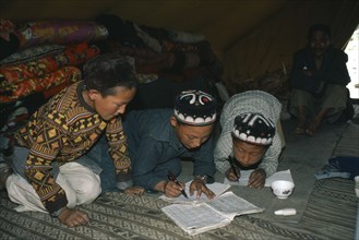 AFGHANISTAN, Tribal People, Kirghiz children writing inside yurt with man sitting beside doorway