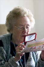 USA, Minnesota, Edina, Elderly woman reading an article with a magnifying lens.