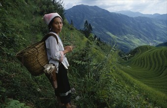 CHINA, Guangxi Province, Longsheng, Woman on steep pathway above rice terraces carrying woven
