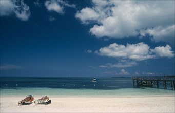 BAHAMAS, Nassau Beach, Two women sunbathing on sandy beach with windsurfer on water beyond.