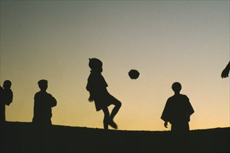 THAILAND, North, Children, Hilltribe kids playing football with a coconut silhouetted against