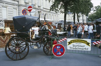 GERMANY, Berlin, Antique carriage at entrance to flea market with people at stalls behind and