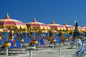 ITALY, Emilia-Romagna, Rimini, "Lines of red, yellow and blue parasols and sun loungers on sandy