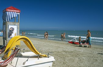 ITALY, Emilia-Romagna, Rimini, Adults and children on sandy beach with pedalo and lifeguard hut in