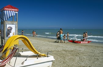 ITALY, Emilia-Romagna, Rimini, Adults and children on sandy beach with pedalo and lifeguard hut in