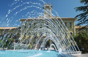 ITALY, Emilia-Romagna, Cattolica, Fountains in town square with building with clock tower behind.