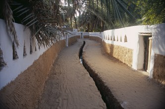 LIBYA, Ghadames, Deep irrigation channel through street between walls partly painted white with