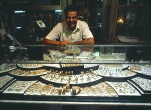 LIBYA, Zawia, Jeweller behind display of gold items in glass topped cabinet.